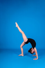 an elegant little gymnast performs a balance exercise on a blue background with a place for text