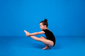 a focused little gymnast performs a balance exercise on a blue background with a place for text