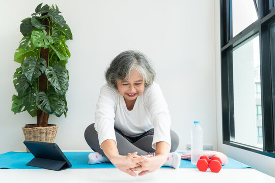 Senior Asian woman watching online courses on a laptop while exercising in the living room at home. Concept of workout training online.