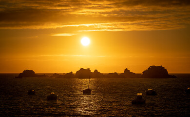 Fototapeta premium Blick von der Atlantikküste bei Plougrescant auf die zerklüfteten Felsen und Fischerboote im Sonnenuntergang, Bretagne, Frankreich