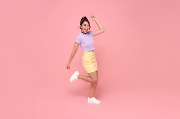 Fototapeta na wymiar Cheerful positive Asian girl jumping in the air with raised fists looking at camera isolated on pink background.