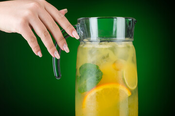 The hand holds a decanter with a cold citrus drink. Summer tropical juice