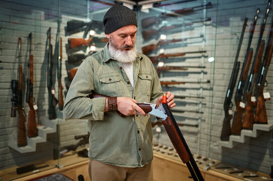 Bearded male hunter loads rifle in gun store