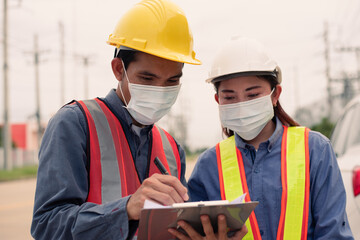 Two engineers wearing yellow and white hats are working in the workplace