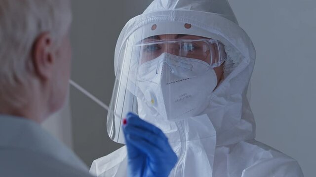 Portrait of woman doctor scientist nurse medic in special uniform transparent protective face shield uses cotton swab equipment to do pcr test old lady taking saliva sample for coronavirus analysis
