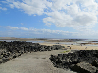 Ponton menant vers le sable normand sous un ciel nuageux blanc et bleu