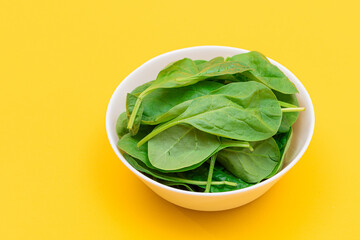Fresh Baby Spinach Leaves in White Bowl on Yellow Background. Vegan and Vegetarian Culture. Raw Food, Green Leaves. Healthy Diet