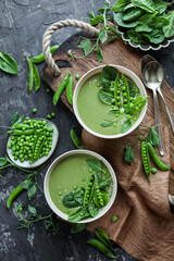 Creamy green pea soup with spinach in beige plates on a wooden tray on a gray table with a tablecloth.