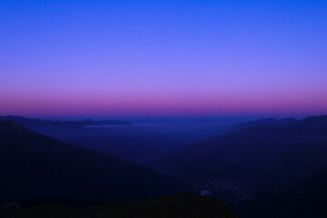 High-altitude view of a mountainous valley. Layer of clouds and pink mist above the mountains at dawn or sunset.