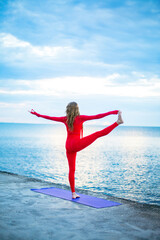 one-legged yoga asana, on the embankment near the sea at dawn with clouds in the sky