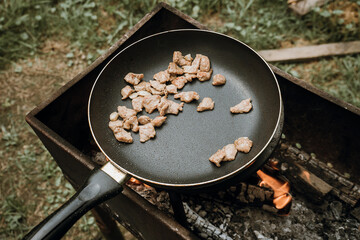 Frying pan of fried bacon, green grass on the background, cooked on the grill on a summer sunny day, summer breakfast, eating in nature.