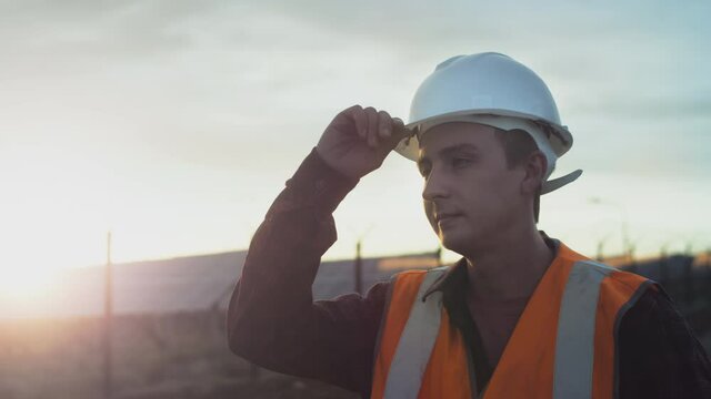 Portrait of a young engineer next to solar panels during sunset. Checks the health and efficiency of renewable energy sources and solar cells. Solar panel plantation. Concept of green energy.