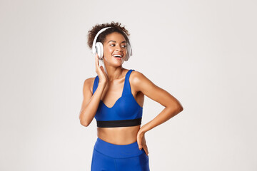 Naklejka na ściany i meble Sport and lifestyle concept. Carefree african-american fitness woman, listening music during workout, exercising in headphones, white background
