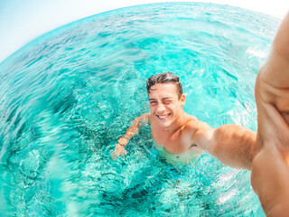 Portrait of happy young man taking a selfie of him in the beach in a blue turquoise water having...