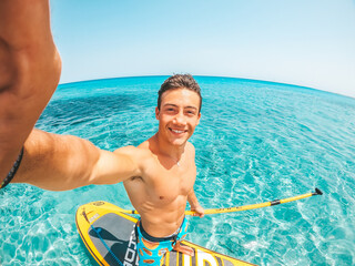 Fototapeta One happy caucasian man enjoying and having fun in vacations outdoors in the beach riding a paddle surf in the water. Attractive boy feeling free traveling.. obraz