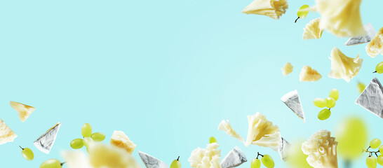 Different kinds of cheeses Blue cheese pieces, Parmesan, brie, camembert, Tete de Moine and grapes flying in the air with crumbs isolated on blue background. mockup for banner with copyspace.