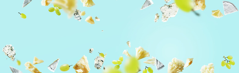 Different kinds of cheeses Blue cheese pieces, Parmesan, brie, camembert, Tete de Moine and grapes flying in the air of frame with crumbs isolated on blue background. Wide banner mockup for menu