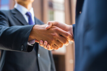 Handshake close-up. Businessman and his colleague are shaking hands in front of modern office building. Financial investors outdoor. Banking and business. - Powered by Adobe