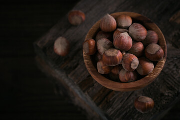 Pile of hazelnuts filbert in a wooden bowl on a dark wooden background