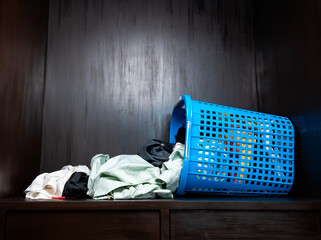 Low light view. A large pile of clothes from a basket that fall on its side in wooden wardrobe.