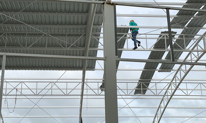 Look up view. Worker climbing on steel structure to thatch the roof of building in the construction site.