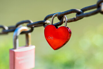 Red heart-shaped padlock hanging on a chain engraved with the sign of infinity.