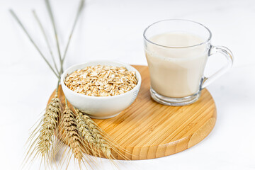 Glass of oat milk with oat flakes on white wooden background
