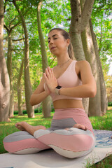 Vertical image of a recognizable young woman doing the pilates starting pose with her hands in prayer position while enjoying a nice day outdoors in the park. Concept of outdoor pilates.