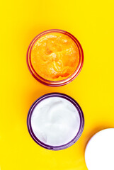 Jars of cream and orange scrub on a yellow background.