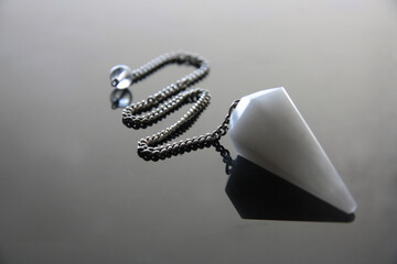 Natural white crystal, aventurine pendulum, with reflection on grey background