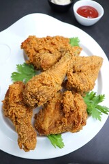 Fresh, hot, crispy deep fried chicken served on a white plate with tomato ketchup and mayonnaise. Chicken snack, hot fried chicken wings. Fast food over moody dark black background with copy space.