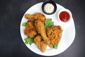 Fresh, hot, crispy deep fried chicken served on a white plate with tomato ketchup and mayonnaise. Chicken snack, hot fried chicken wings. Fast food over moody dark black background with copy space.