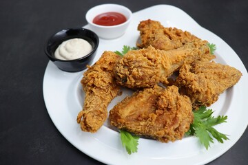 Fresh, hot, crispy deep fried chicken served on a white plate with tomato ketchup and mayonnaise. Chicken snack, hot fried chicken wings. Fast food over moody dark black background with copy space.