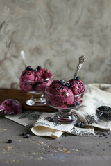 Blueberry ice cream, garnished with berries and black sesame seeds, in glass bowls with spoons on a dark gray table. Cold summer desserts.