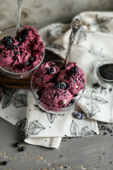 Blueberry ice cream, garnished with berries and black sesame seeds, in glass bowls with spoons on a dark gray table. Cold summer desserts.