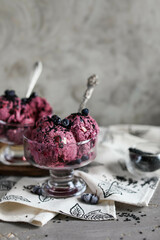 Blueberry ice cream, garnished with berries and black sesame seeds, in glass bowls with spoons on a dark gray table. Cold summer desserts.