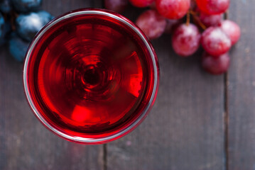 glass of red wine and grapes on black wooden table background