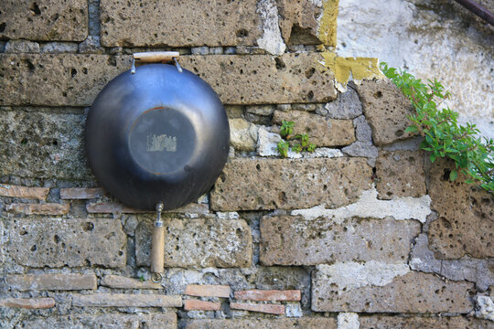 A rusty cast iron frying pan hangs outside, on an old wall of rustic house. © Pamela Ranya