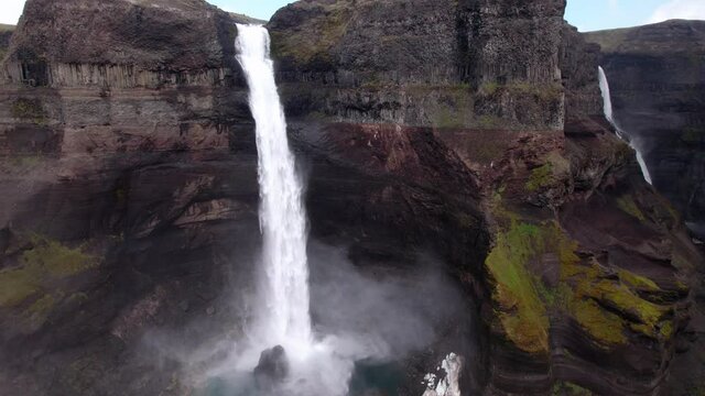 Slowly rising and turning aerial drone shot of waterfall. Begins low and pans up. Beautiful canyon scene.