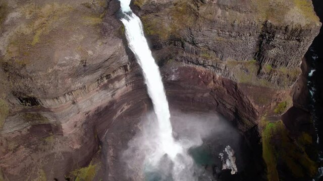 Revolving drone shot looking down at a tall waterfall. Clouds move in and cause drastic change in scene. Steep cliffs, epic scenery. 