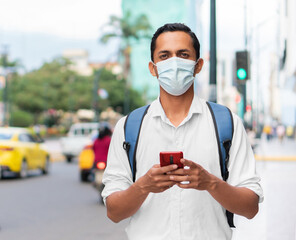 Hispanic young student using disposable mask while holding a red cell phone.