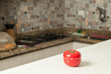 Red tomato-shaped kitchen timer with cooking in the background. To let you know when to turn off the stove and food is ready. Brazilian cuisine. Kitchen concept. Household appliance concept.
