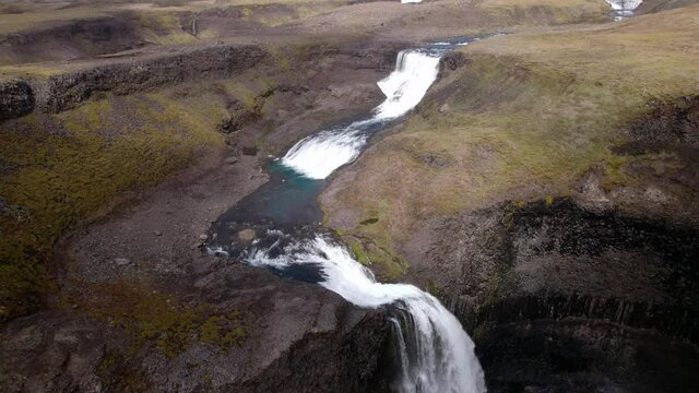 Aerial shot at the top of waterfalls, with fast moving clouds creating shadows. Dramatic change. Revolving and turning shot, in Iceland.
