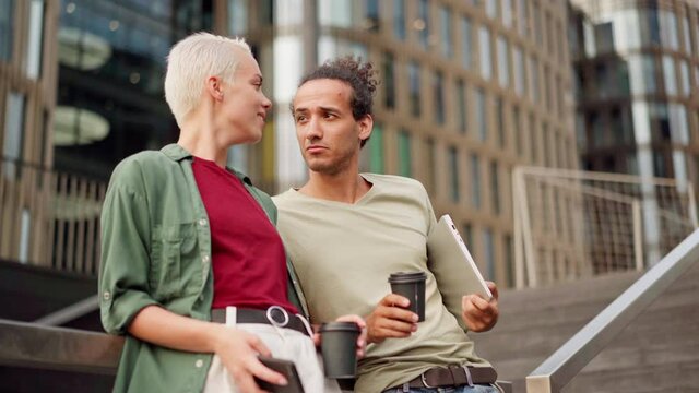 Zoom In Side View Of Young Couple, Two Friends, Colleagues Or Fellow Students Standing On Staircase In City Center Leaning On Railing And Talking Over Takeaway Coffee At Break Or After Work