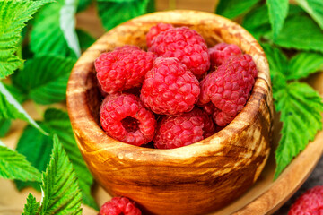 Fresh juicy raspberries in wooden bowl. Summer still life with raspberries on an old wooden table. Copy space .Jar of raspberry jam and fresh berries on wooden background