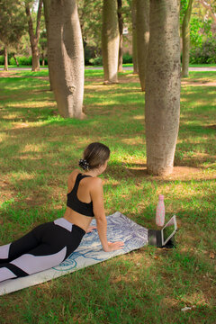 Vertical image of a young girl doing the cobra pose while she is relaxing outdoors in the park. Concept of outdoor pilates 2021.