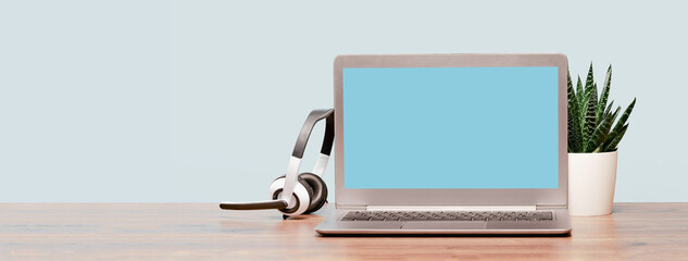 Laptop. Mockup screen and headphones on wooden desk and plain background banner. Distant learning. working from home, online courses or support minimal concept. Helpdesk or call center headset
