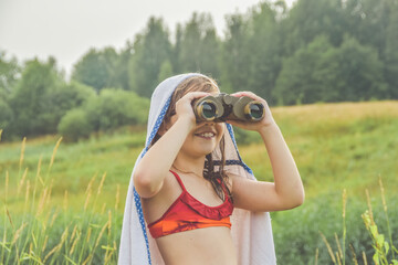 a child girl stands in a meadow and looks through binoculars