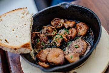 A pan of champignon or other mushrooms and a slice of bread on a wooden board.