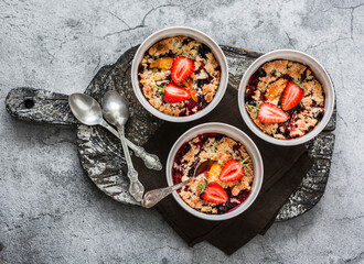 Plum, nectarines, black currant, strawberry crumble in portion forms on a wooden rustic cutting board on a gray background, top view
